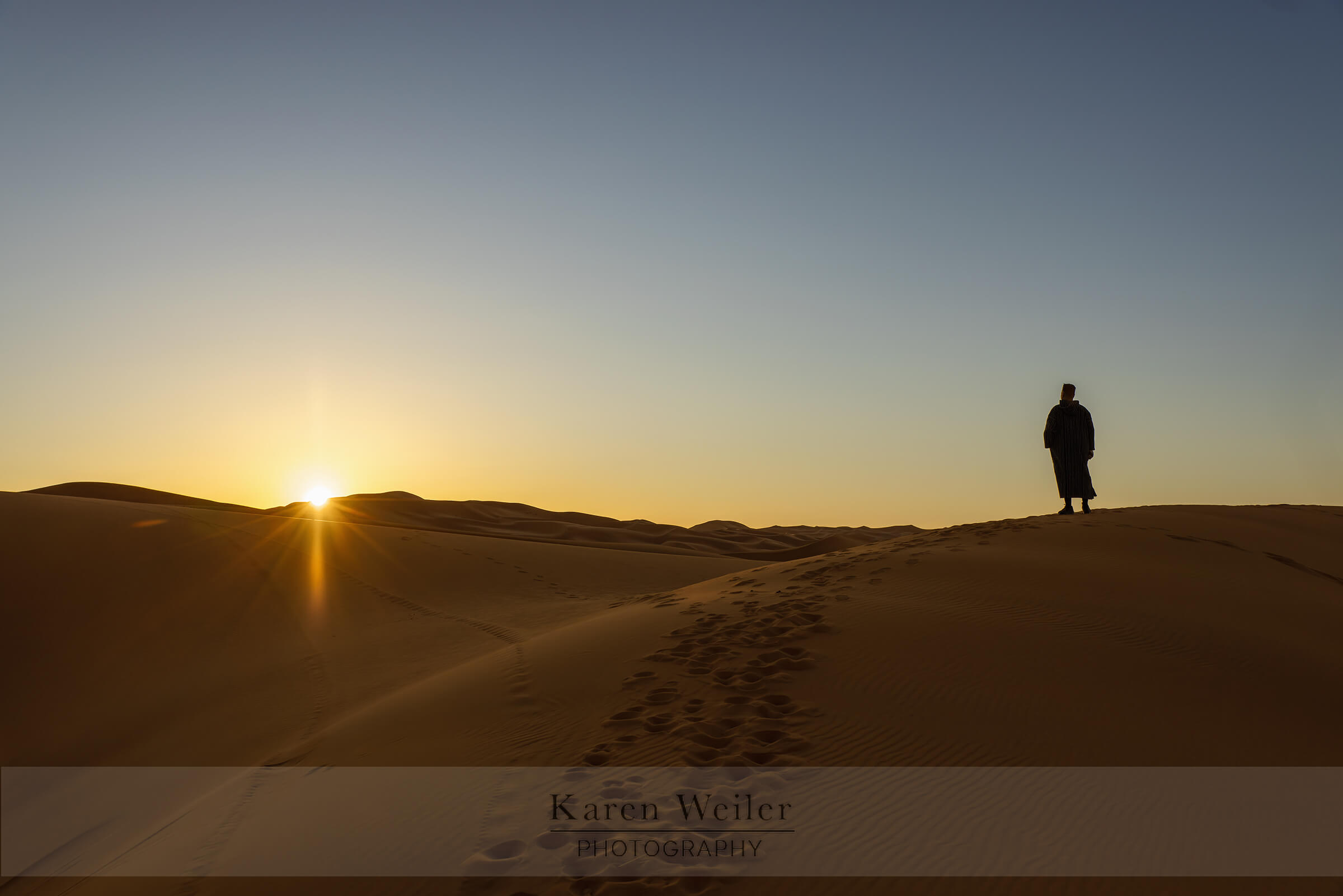 Man stands watching sunrise over Sahara Desert dunes